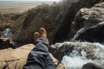 Pernas de corte de macho sentado no topo da montanha perto de cachoeira em roupas de inverno — Fotografia de Stock
