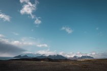 Paisaje de campo y montañas nevadas bajo cielo azul y nubes blancas, Islandia - foto de stock