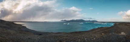 Vista panorámica de la costa con montañas cubiertas de nieve en el fondo, Islandia - foto de stock