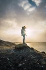 Жінка стоїть на скелі з видом на море і хмари на сонячному світлі — стокове фото