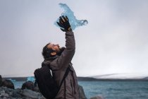 Людина сидить на узбережжі з шматочком льоду над головою — стокове фото