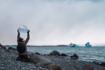 Mann sitzt an Küste mit Stück Eis über dem Kopf — Stockfoto