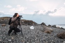 Homem definindo equipamentos fotográficos na costa fria — Fotografia de Stock