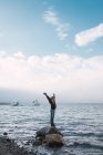 Woman balancing on rock in sea with outstretched arms — Stock Photo