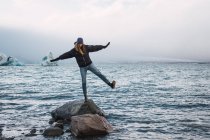 Donna in equilibrio sulla roccia in acqua fredda blu di mare con blocchi di ghiaccio sullo sfondo, Islanda — Foto stock