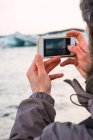 Close-up of male hands taking photo of cold beach with smartphone — Stock Photo