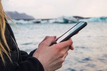 Close-up de mãos femininas usando smartphone na costa do mar frio — Fotografia de Stock