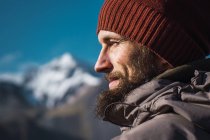 Улыбающийся бородатый мужчина в шляпе смотрит вдаль на природу — стоковое фото