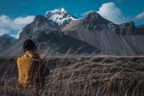 Mujer sentada en el suelo y mirando montañas remotas, Islandia - foto de stock