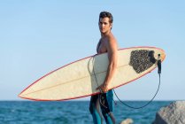 Человек с доской для серфинга стоит на берегу — стоковое фото