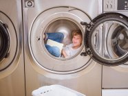 Elementary age boy lying inside washing machine and reading book. — Stock Photo