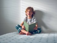 Niño en pijama leyendo libro - foto de stock