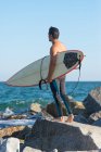 Uomo con tavola da surf in piedi sulla costa — Foto stock