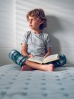 Хлопчик сидить на ліжку з книгою — стокове фото