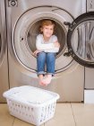 Lindo niño de edad elemental sentado dentro de la lavadora y mirando en la cámara . - foto de stock