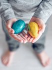 Vista recortada de un niño irreconocible sosteniendo huevos de chocolate dorados y azules . - foto de stock