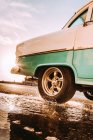 Primer plano de brillante vintage azul y rosa coche de conducción en la carretera y salpicaduras de agua en charco en retroiluminación - foto de stock