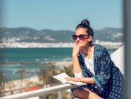 Jeune femme relaxante avec livre au balcon en bord de mer . — Photo de stock