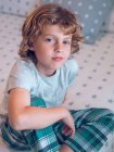 Charming boy in pajamas sitting on bed — Stock Photo