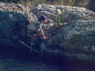 Boy climbing on rock with fishing rod — Stock Photo
