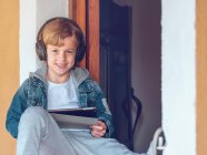 Boy in headphones with tablet leaning on wall — Stock Photo