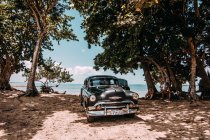 LA HABANA, CUBA - MAY 1, 2018: black retro car parked on sandy tropical coastline of Cuba in sunlight — Stock Photo