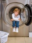 Mignon garçon d'âge préscolaire assis à l'intérieur de la machine à laver et regardant à la caméra . — Photo de stock