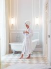 Femme en peignoir avec flacon dans la salle de bain — Photo de stock