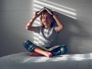 Мальчик с книгами на голове и коленях — стоковое фото