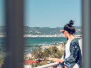 Young woman relaxing with book and looking at view at balcony by seaside. — Stock Photo