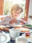 Little boy with cup sitting at table — Stock Photo