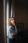 Young woman standing at window — Stock Photo