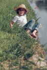 Menino sentado na grama no rio — Fotografia de Stock