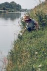 Мальчик, сидящий в траве у реки — стоковое фото