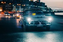 Винтажные автомобили едут по дороге в освещенном городе в сумерках, Куба — стоковое фото