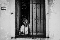 La habana, kuba - 1. Mai 2018: Schwarz-Weiß-Aufnahme eines älteren Mannes in einem Fenster mit Metallstangen, der auf der Straße wegschaut, kuba. — Stockfoto