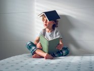 Niño con libros en la cabeza y regazo - foto de stock