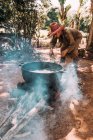 LA HABANA, CUBA - MAY 1, 2018: Ethnic man on remote country yard in tropical jungles of Cuba heating water in big boiler — Stock Photo