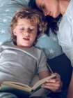 Madre durmiendo e hijo leyendo libro - foto de stock