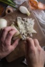 Human hands cutting fresh onion on wooden chopping board — Stock Photo