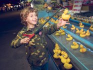 Вид сбоку веселый мальчик, стоящий на аттракционе и ловящий утиные игрушки — стоковое фото