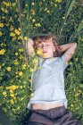Vista aérea del niño acostado en el prado verde con flores amarillas con los ojos cerrados . - foto de stock