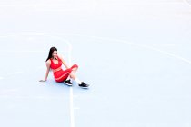 Femme en costume de sport rouge vif assis sur fond bleu clair — Photo de stock