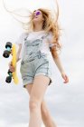 Chica rubia con penny board caminando en el parque - foto de stock