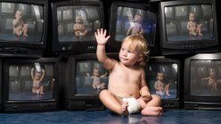 Маленький хлопчик сидить з рукою на старовинних телевізорах — стокове фото