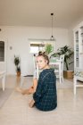 Young woman in checkered shirt sitting on floor in stylish room and looking at camera — Stock Photo