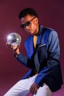 Trendy party young man with disco ball on dark purple background — Stock Photo