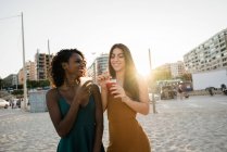 Young women enjoying drinks on sandy town beach in backlit — Stock Photo