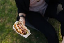 Femme tenant un hamburger assis sur l'herbe — Photo de stock
