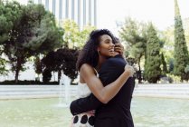 Charming multiracial couple embracing while standing near fountain in park — Stock Photo